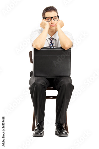 Photo: Sad male with leather suitcase sitting on a wooden chair Sad male with leather suitcase sitting on a wooden chair