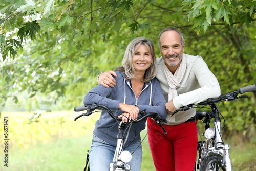 Photo: Cheerful senior couple with bicycle in country path Cheerful senior couple with bicycle in country path