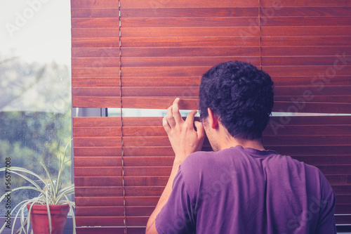 Photo: Young man peeping out through venetian blinds Young man peeping out through venetian blinds