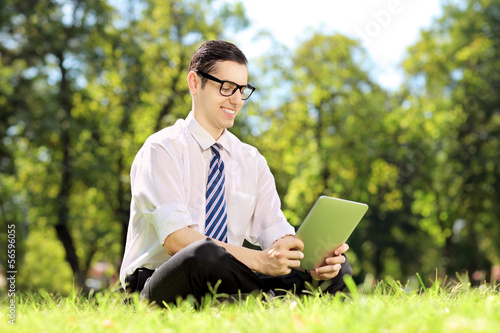 Photo: Businessperson with glasses seated on a grass working on tablet Businessperson with glasses seated on a grass working on tablet