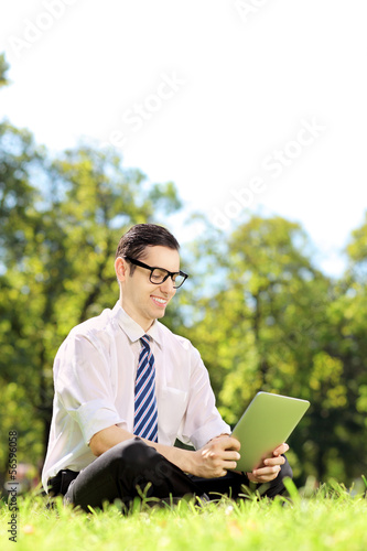 Photo: Young businessperson sitting on a grass and working on a tablet Young businessperson sitting on a grass and working on a tablet