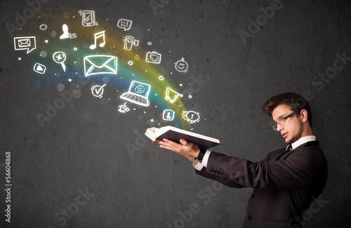 Photo: Young businessman reading a book with multimedia icons coming ou Young businessman reading a book with multimedia icons coming ou
