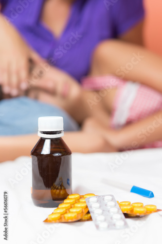 Photo: Pills and thermometer with a sick girl in the background Pills and thermometer with a sick girl in the background