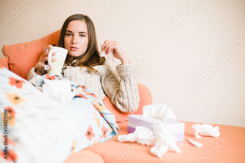 Photo: Young woman with cold / flu lying on couch and drinking tea Young woman with cold / flu lying on couch and drinking tea