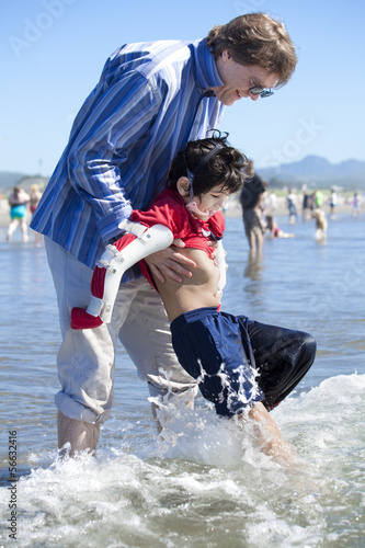 Photo: Father helping disabled son walk in the ocean waves on beach Father helping disabled son walk in the ocean waves on beach