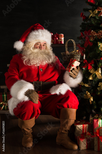 Photo: Santa placing gifts under Christmas tree in dark room Santa placing gifts under Christmas tree in dark room