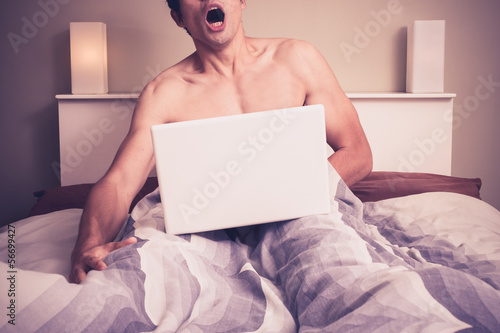 Photo: Young man is sitting in bed and watching pornography on laptop Young man is sitting in bed and watching pornography on laptop