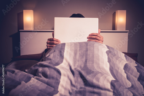 Photo: Man is sitting in bed behind his laptop Man is sitting in bed behind his laptop
