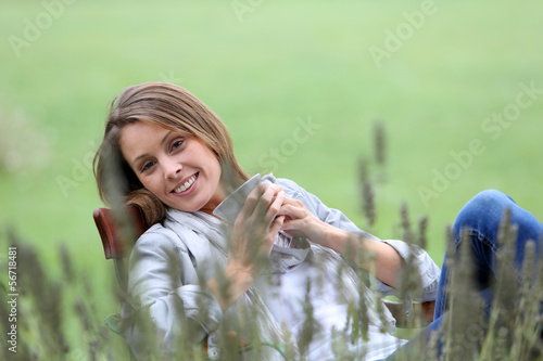 Photo: Beautiful smiling woman drinking hot drink in garden Beautiful smiling woman drinking hot drink in garden
