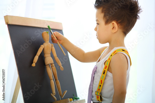 Photo: A little boy paints the wooden man near easel A little boy paints the wooden man near easel