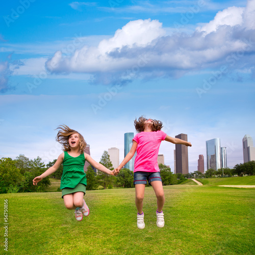 Photo: Two girls friends jumping happy holding hand in city skyline Two girls friends jumping happy holding hand in city skyline