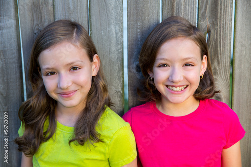 Photo: Happy twin sisters smiling on wood backyard fence Happy twin sisters smiling on wood backyard fence