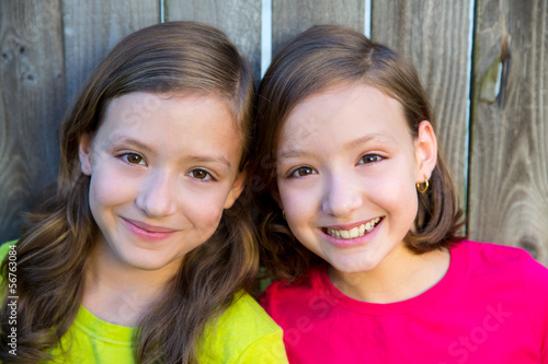 Photo: Happy twin sisters smiling on wood backyard fence Happy twin sisters smiling on wood backyard fence