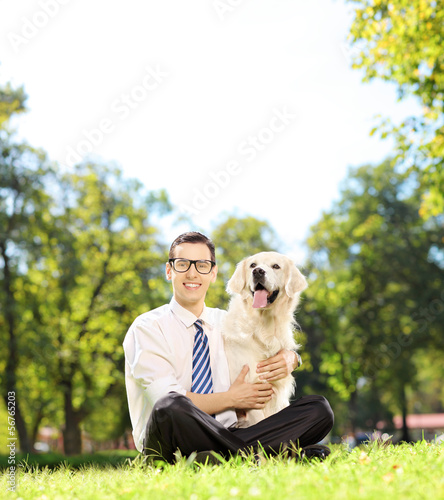 Photo: Man sitting on a grass and hugging his labrador retriever dog Man sitting on a grass and hugging his labrador retriever dog