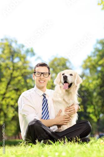 Photo: Smiling male sitting on a grass and hugging his dog in a park Smiling male sitting on a grass and hugging his dog in a park