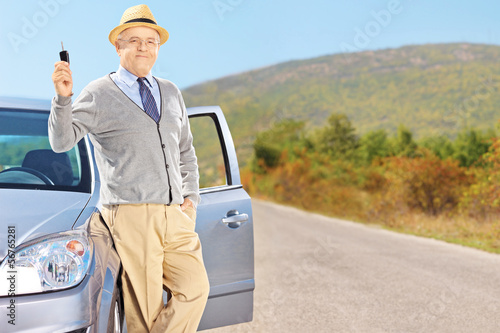 Photo: Smiling senior male holding a car key next to his automobile Smiling senior male holding a car key next to his automobile