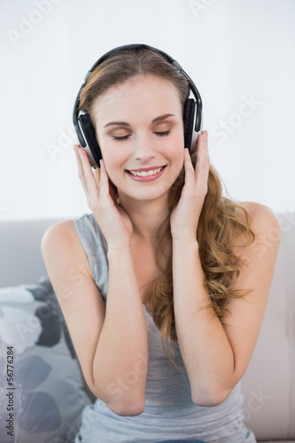 Photo: Content young woman sitting on sofa listening to music Content young woman sitting on sofa listening to music