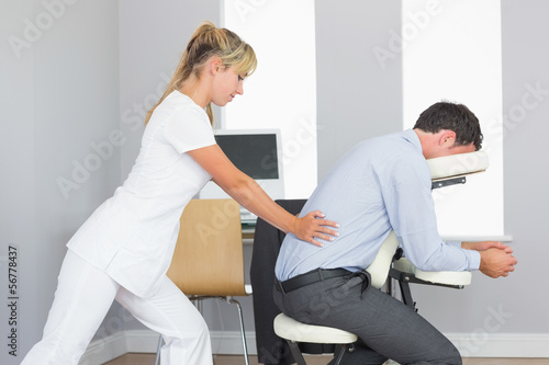 Photo: Masseuse treating clients lower back in massage chair Masseuse treating clients lower back in massage chair