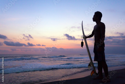 Photo: Indonesian surfer standing at sunset in Ocean in Bali, Indonesia Indonesian surfer standing at sunset in Ocean in Bali, Indonesia