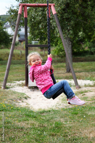 Photo: Happy toddler girl on a swing in city park Happy toddler girl on a swing in city park