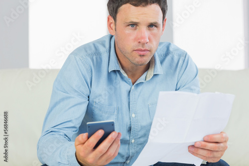 Photo: Serious casual man holding calculator and document Serious casual man holding calculator and document