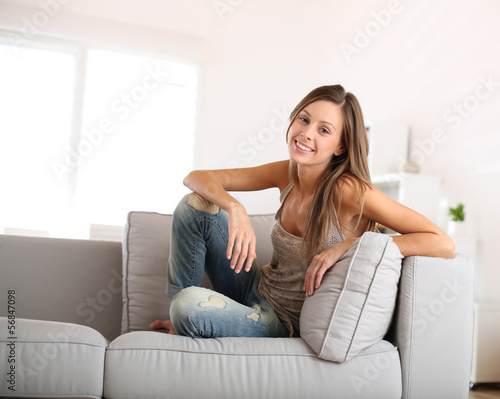 Photo: Beautiful young woman sitting in couch at home Beautiful young woman sitting in couch at home
