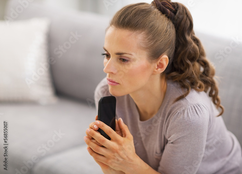 Photo: Concerned young woman sitting on sofa and holding mobile phone Concerned young woman sitting on sofa and holding mobile phone