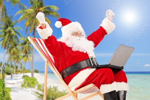 Photo: Happy Santa Claus sitting on a chair with laptop and gesturing Happy Santa Claus sitting on a chair with laptop and gesturing