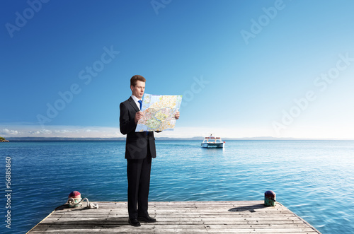 Photo: Business man standing on pier with map in hands Business man standing on pier with map in hands