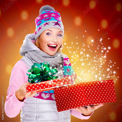 Photo: Surprised woman with a christmas gift with magic shining from b Surprised woman with a christmas gift with magic shining from b
