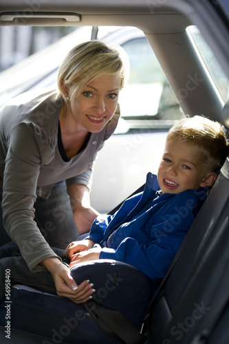 Photo: Mother putting son in car seat. Mother putting son in car seat.