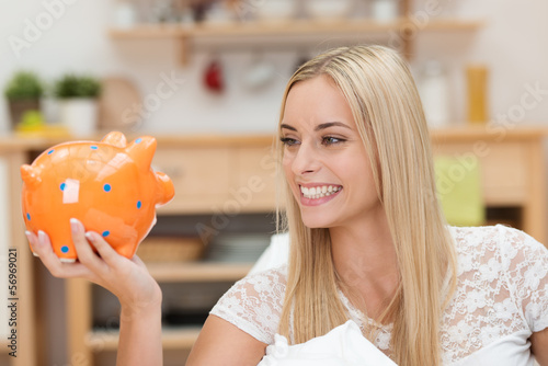 Photo: blonde junge frau schaut lächelnd auf ihr sparschwein blonde junge frau schaut lächelnd auf ihr sparschwein
