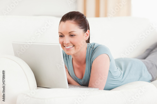 Photo: Attractive woman relaxing with her laptop while lying on a sofa Attractive woman relaxing with her laptop while lying on a sofa