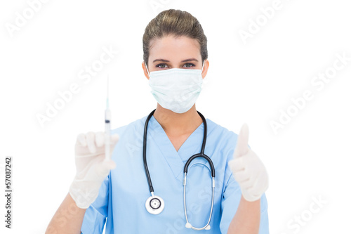 Photo: Beautiful brown haired nurse in blue scrubs holding a syringe an Beautiful brown haired nurse in blue scrubs holding a syringe an