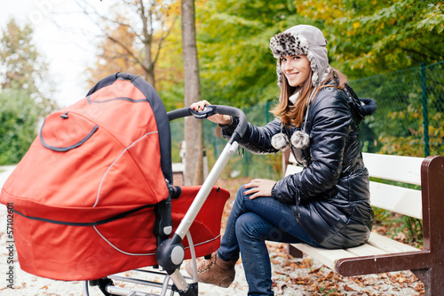 Photo: Young woman sitting on park bench with baby in stroller Young woman sitting on park bench with baby in stroller