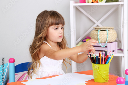Photo: Little girl draws sitting at table in room Little girl draws sitting at table in room