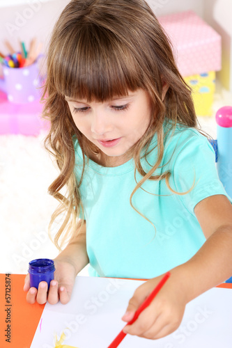 Photo: Little girl draws sitting at table in room on shelves Little girl draws sitting at table in room on shelves