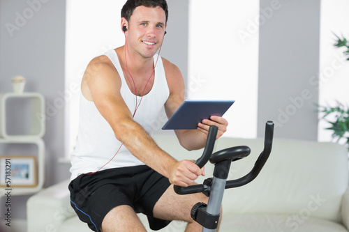 Photo: Smiling sporty man exercising on bike and holding tablet Smiling sporty man exercising on bike and holding tablet
