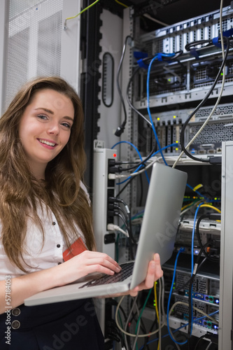 Photo: Woman happily using laptop to work on servers Woman happily using laptop to work on servers