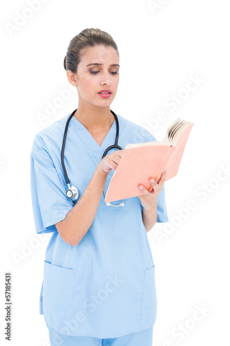 Photo: Worried brown haired nurse in blue scrubs reading a book Worried brown haired nurse in blue scrubs reading a book