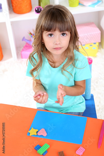 Photo: Little girl molds from plasticine sitting at table in room Little girl molds from plasticine sitting at table in room