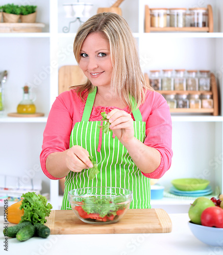 Photo: Happy smiling woman in kitchen preparing vegetable salad Happy smiling woman in kitchen preparing vegetable salad