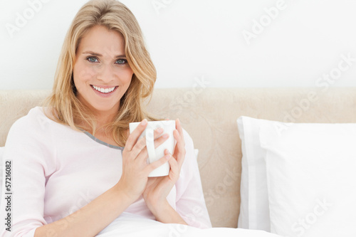 Photo: Woman sitting in bed with a cup in her hands looking forward and Woman sitting in bed with a cup in her hands looking forward and