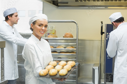 Photo: Cute young female baker holding a baking tray with rolls on it Cute young female baker holding a baking tray with rolls on it