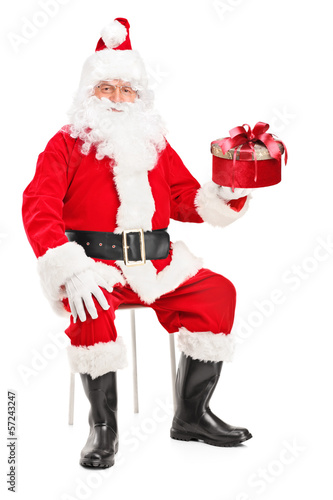 Photo: Smiling Santa Claus on a chair holding a present Smiling Santa Claus on a chair holding a present