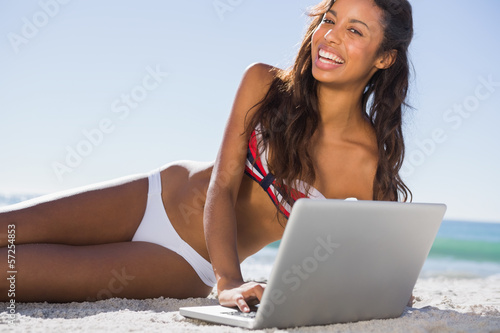 Photo: Happy attractive young woman in bikini with her laptop Happy attractive young woman in bikini with her laptop
