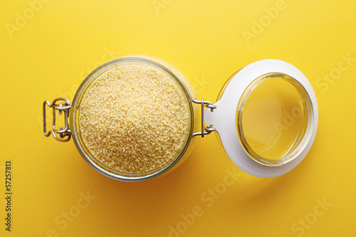 Photo: Raw cous cous on a glass jar on yellow background Raw cous cous on a glass jar on yellow background