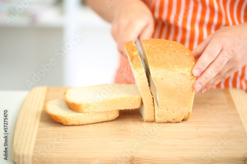 Photo: Woman slicing bread on chopping board, close up Woman slicing bread on chopping board, close up