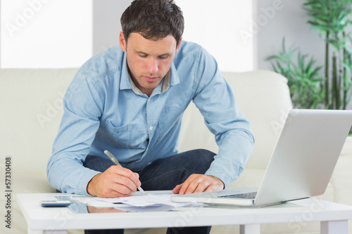 Photo: Serious casual man writing on sheets paying bills Serious casual man writing on sheets paying bills