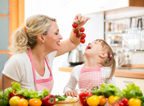 Photo: mother preparing dinner and feeding kid tomato in kitchen mother preparing dinner and feeding kid tomato in kitchen